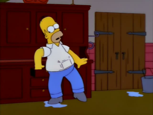 Homer stands in a kitchen beside a red hutch cabinet with a closed wooden door and a bucket behind him