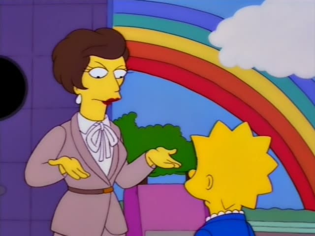 Lisa Simpson stands facing a woman with a short brown bouffant, tan suit and white bow blouse in front of a rainbow painted…
