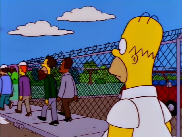 Homer stands on a sidewalk beside a chain-link fence topped with razor wire and watches a group of men walk away: a man…