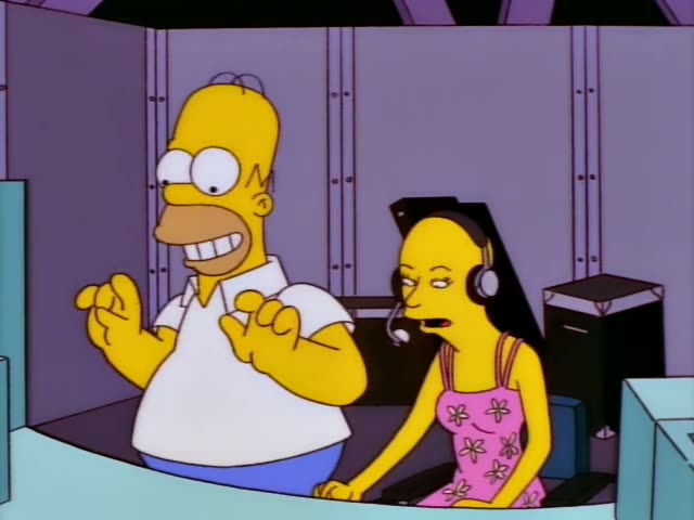 Homer Simpson stands and sits at a console in a purple-walled control booth beside a long-haired woman in a pink flowered…