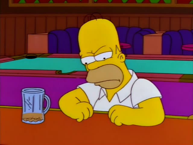 Homer Simpson sits at the bar with a nearly empty mug in front of him, grimacing, gritting his teeth and gesturing as he…