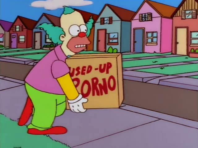 Krusty the Clown lugs a cardboard box labeled "Used-Up Porno" along a suburban sidewalk lined with colorful houses…
