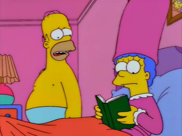 Homer stands beside a bed while Marge sits propped up holding an open green book