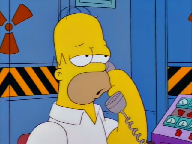 Homer Simpson sits in a control room with blue cabinets marked by radiation symbols and yellow-black hazard stripes…