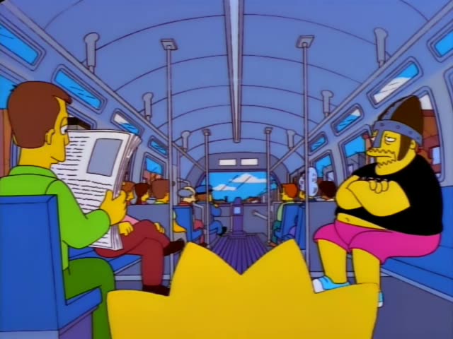 Lisa sits in the foreground of a train car, while a man in a green sweater reads a newspaper on the left and a bearded man…