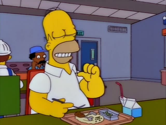 Homer Simpson sits at a cafeteria table with a lunch tray holding food, a carton of milk with a straw, and a plastic…