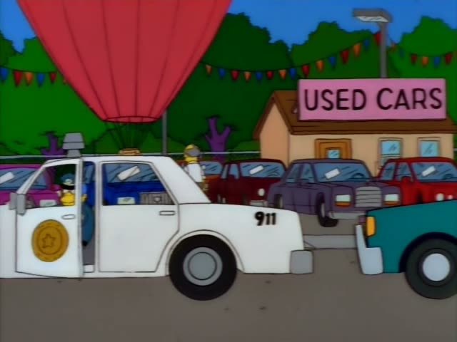 Chief Wiggum stands beside a white police car marked 911 at a used car lot, gesturing and holding a gun while two officers…