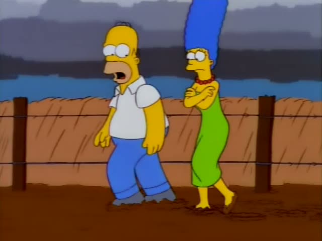 Homer and Marge walk along a muddy path beside a wooden fence strung with barbed wire, with a grey sky and a blue lake…