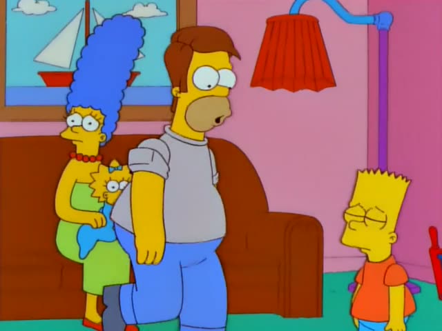 Homer Simpson stands in the living room with Marge, who holds baby Maggie, and Lisa in her red dress while Bart in an orange…