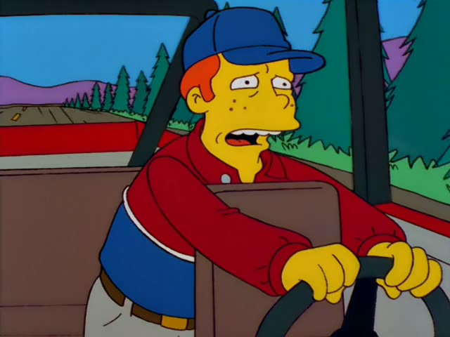 Homer Simpson grips the steering wheel of a mint-green motorhome, wide-eyed and grimacing, while a tall blonde woman…