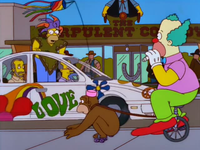 Homer sits behind the wheel of a white psychedelic car with flower designs and LOVE lettering, while Marge stands beside it…