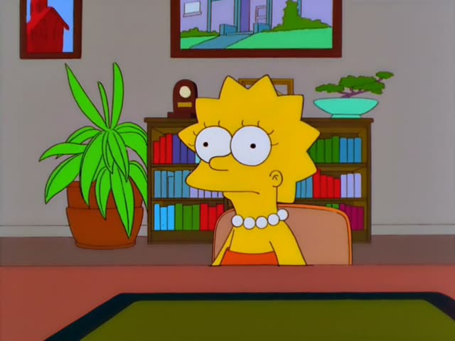 Lisa sits at a desk in a room with bookshelves, a potted plant, a bonsai and a mantel clock, first staring with wide eyes…