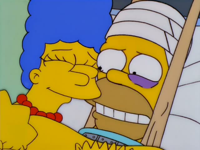 Homer lies in a hospital bed while Marge hugs him with her eyes closed and smiling