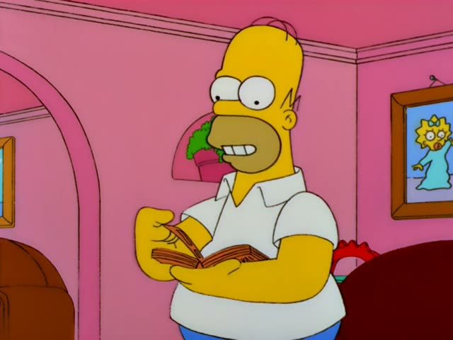 Homer Simpson stands in the pink living room beside a red armchair, holding a folded pamphlet and munching on leafy greens…