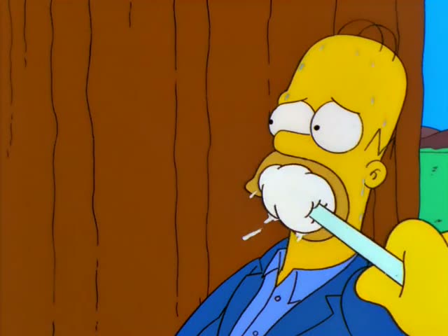 Homer is chained to a giant redwood trunk in a forest, with Marge in a pink dress chained to a nearby tree and Chief Wiggum…