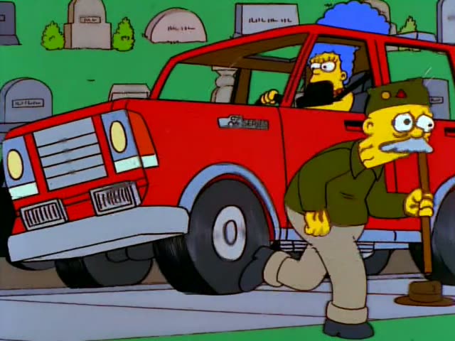 Herb runs along a cemetery road past a lavender car while a black-haired man in a white jacket leans out of its window…