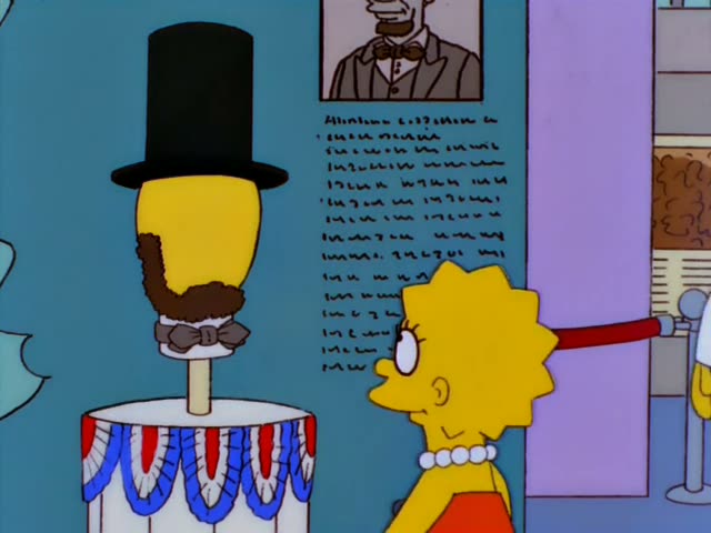 Lisa stands beside an animatronic Abraham Lincoln figure, a yellow head in a black top hat with a brown beard and bow tie…