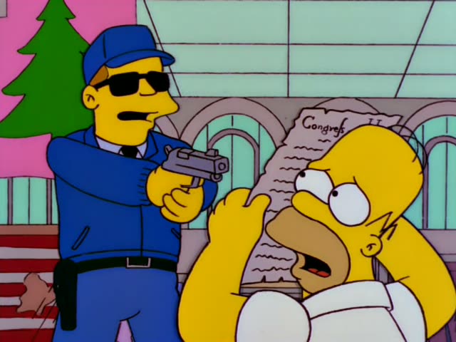 Homer Simpson stands in a building with a Christmas tree and an American flag, clutching a document labeled 'Congress'…