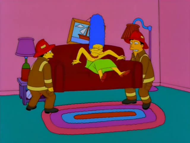 Two firefighters carry a large red couch across a living room with pink walls, a purple side table with a lamp, a framed…