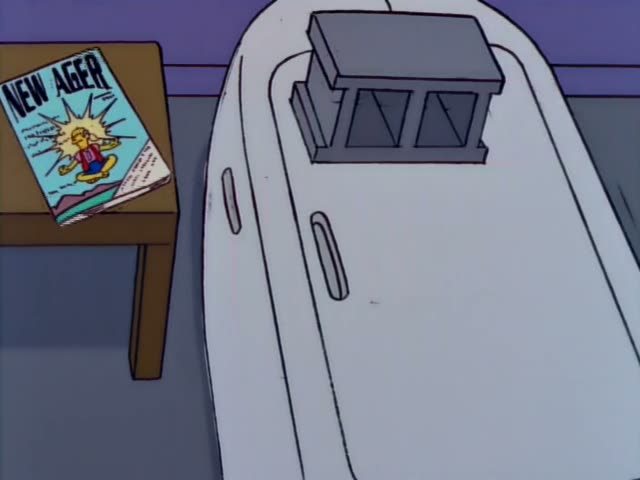 Homer appears with a sullen look against a plain blue background while a large white rounded object sits beside a wooden…