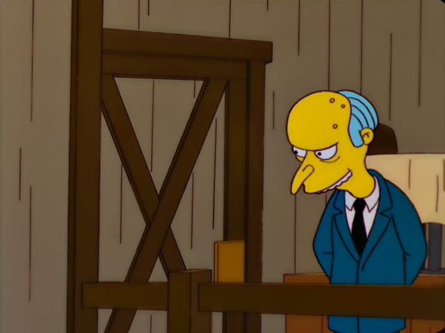 Mr. Burns stands behind a wooden counter in a blue suit and black tie, smirking, while a thin-faced man with short brown…
