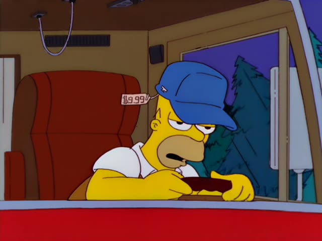 Homer Simpson sits in the driver's seat of a vehicle with a red seat and red dashboard, pine trees visible through the side…