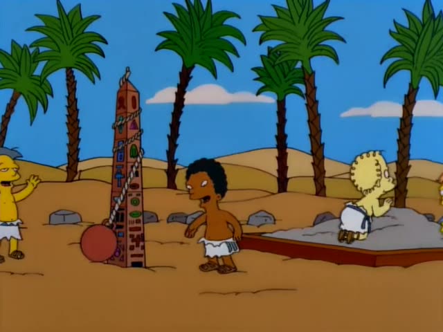 Carl stands in a sandy desert with palm trees beside a grey-haired man who gestures near a red ball and a brick obelisk…